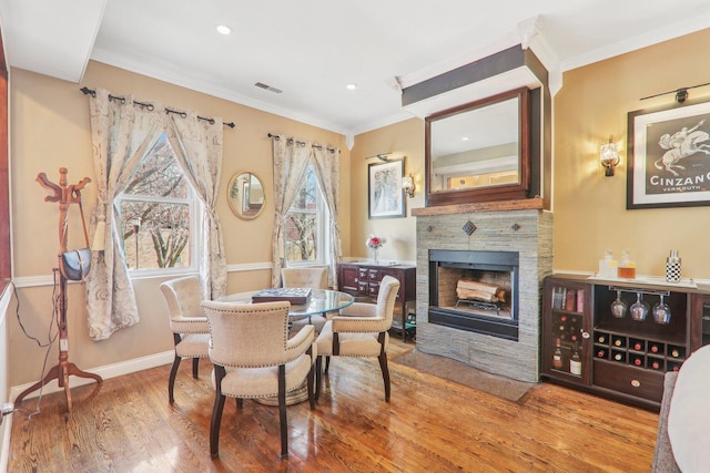 dining area with wood finished floors, recessed lighting, a fireplace, crown molding, and baseboards