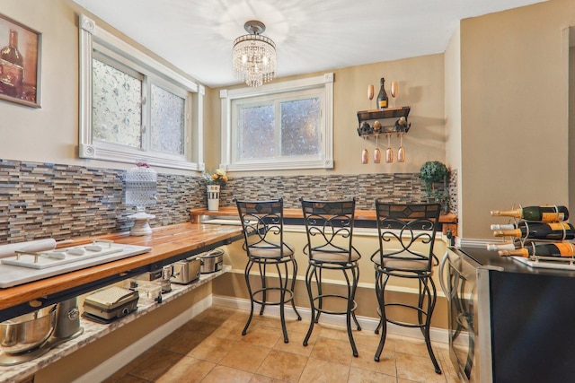 interior space featuring light tile patterned floors, baseboards, butcher block counters, decorative backsplash, and a chandelier