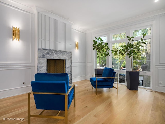 sitting room featuring a decorative wall, wood finished floors, a high end fireplace, and ornamental molding