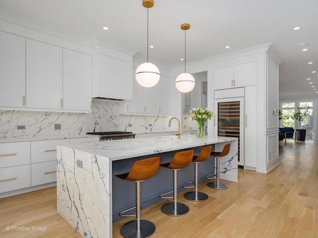 kitchen featuring white cabinets, an island with sink, backsplash, and a sink