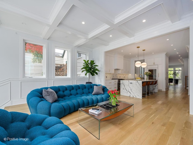 living room with beam ceiling, a decorative wall, light wood-style floors, and coffered ceiling