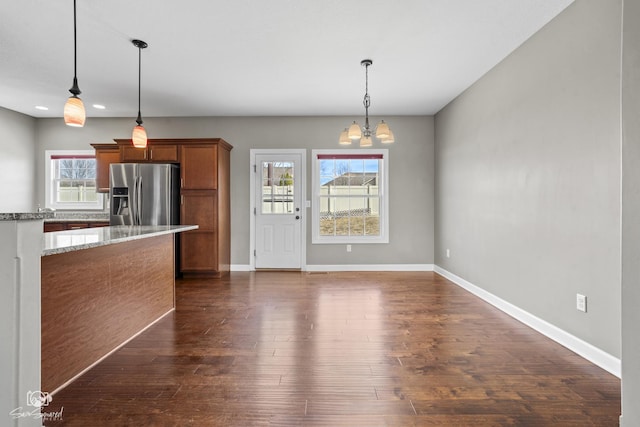 kitchen featuring light stone counters, dark wood finished floors, brown cabinetry, stainless steel fridge with ice dispenser, and a chandelier