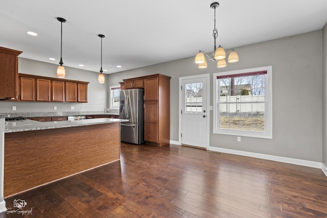 kitchen with stainless steel fridge with ice dispenser, dark wood finished floors, light stone counters, recessed lighting, and brown cabinets