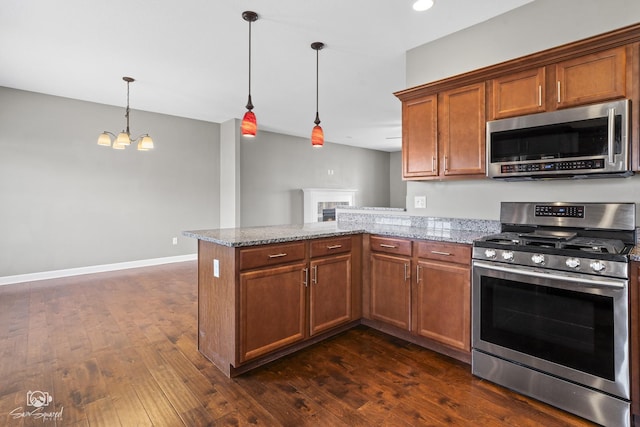 kitchen with appliances with stainless steel finishes, a peninsula, brown cabinetry, light stone countertops, and dark wood-style flooring