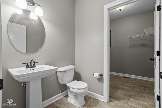 bathroom with a spacious closet, toilet, baseboards, and a sink