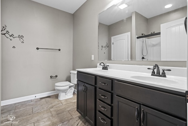 bathroom with double vanity, toilet, baseboards, and a sink