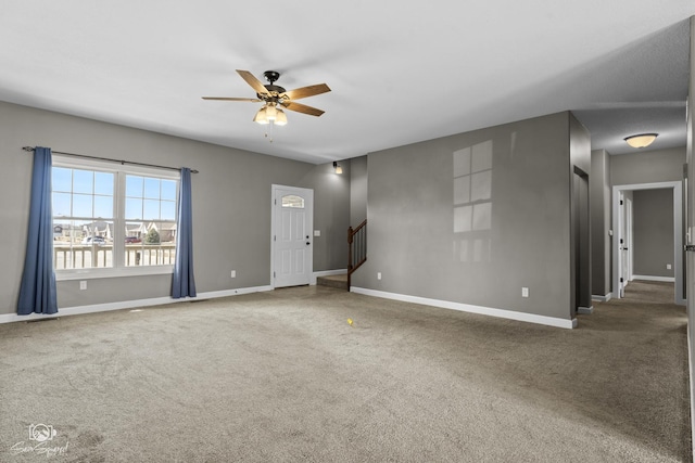 carpeted spare room with stairway, baseboards, and ceiling fan