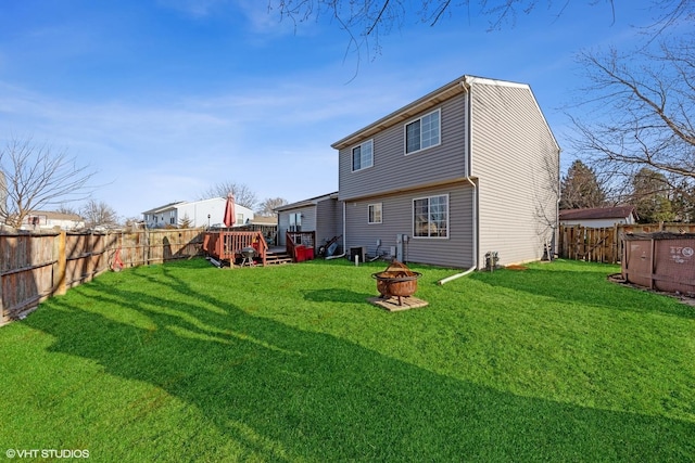 rear view of property featuring a wooden deck, a fire pit, a fenced backyard, and a lawn