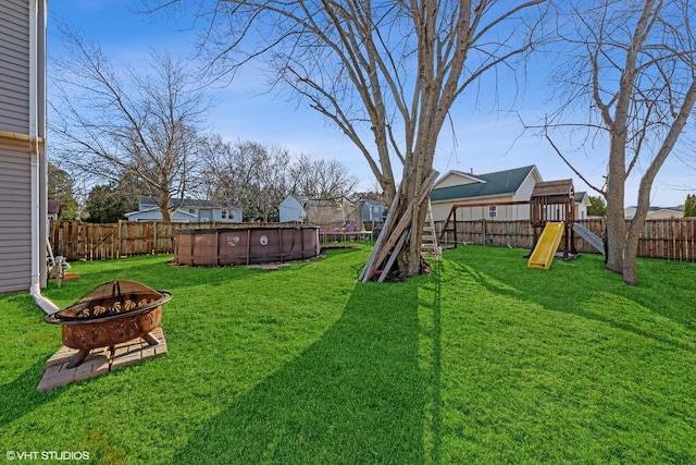 view of yard with a fenced in pool, a fire pit, a playground, and a fenced backyard