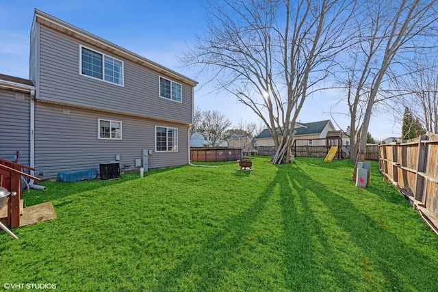 rear view of property featuring a yard, central AC unit, a fenced backyard, and a playground