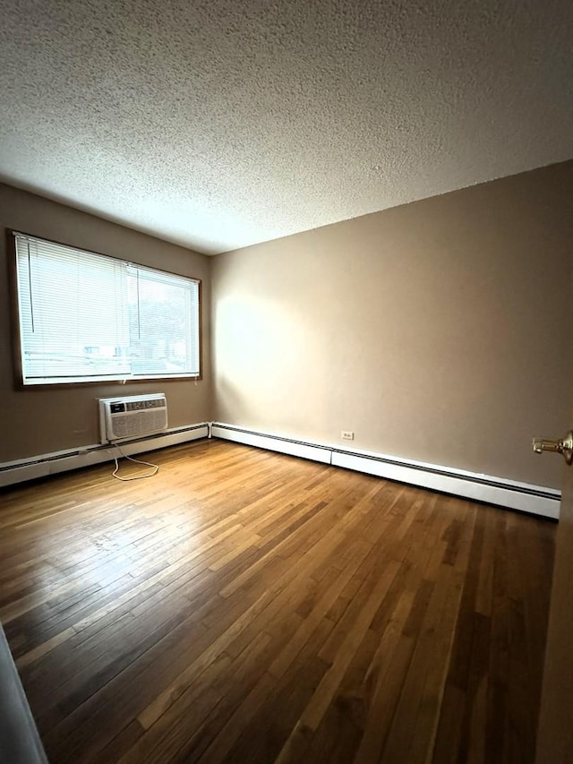 empty room with a baseboard heating unit, wood-type flooring, a wall mounted air conditioner, and a textured ceiling