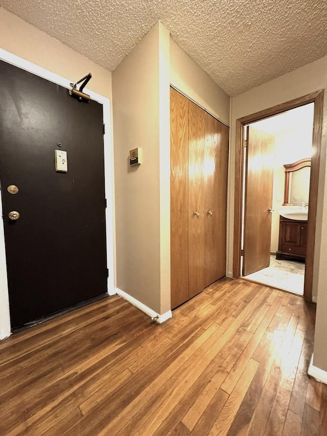 hallway with a sink, a textured ceiling, baseboards, and hardwood / wood-style floors