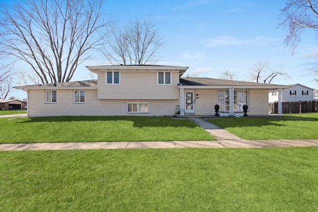 tri-level home with brick siding, a front lawn, and fence