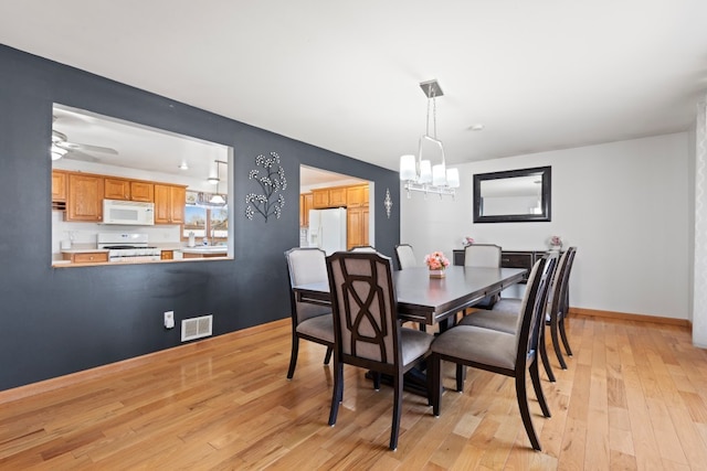 dining space featuring visible vents, light wood-style flooring, ceiling fan with notable chandelier, and baseboards