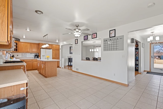 kitchen with ceiling fan with notable chandelier, a kitchen island, white refrigerator with ice dispenser, light countertops, and baseboards