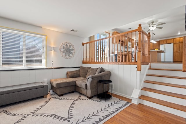 living room featuring stairs, visible vents, light wood-type flooring, and a ceiling fan