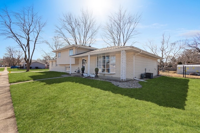 split level home featuring a front lawn, central air condition unit, fence, and brick siding