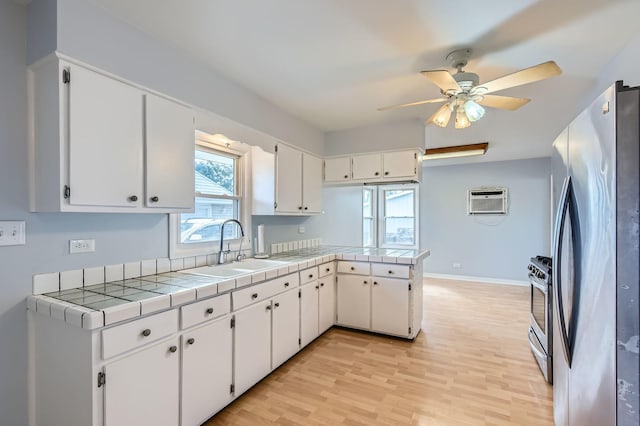 kitchen with light wood finished floors, an AC wall unit, a peninsula, white cabinets, and stainless steel appliances