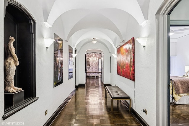 hallway with baseboards, a notable chandelier, and vaulted ceiling