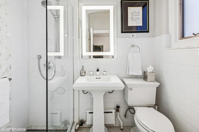 bathroom featuring a sink, tiled shower, toilet, and tile walls