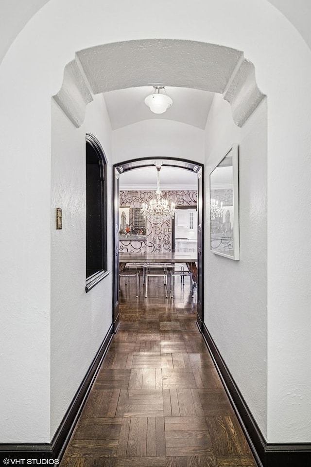 hall featuring baseboards, lofted ceiling, arched walkways, a notable chandelier, and a textured wall