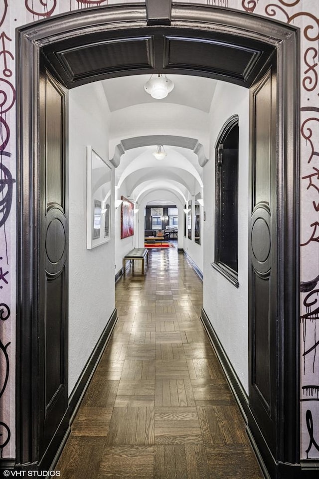 hallway featuring arched walkways, baseboards, and vaulted ceiling