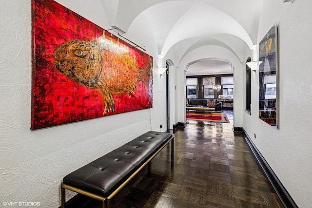 corridor with baseboards, arched walkways, and a textured wall