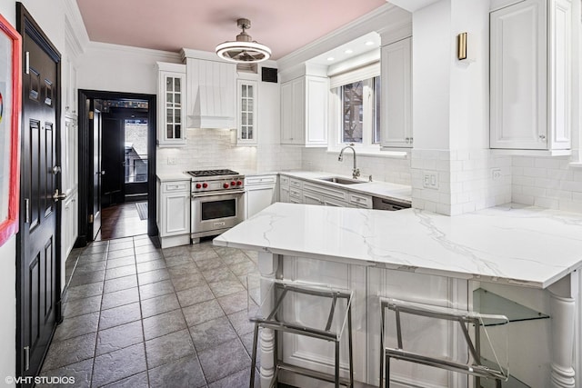 kitchen featuring a breakfast bar area, a peninsula, a sink, white cabinets, and premium range