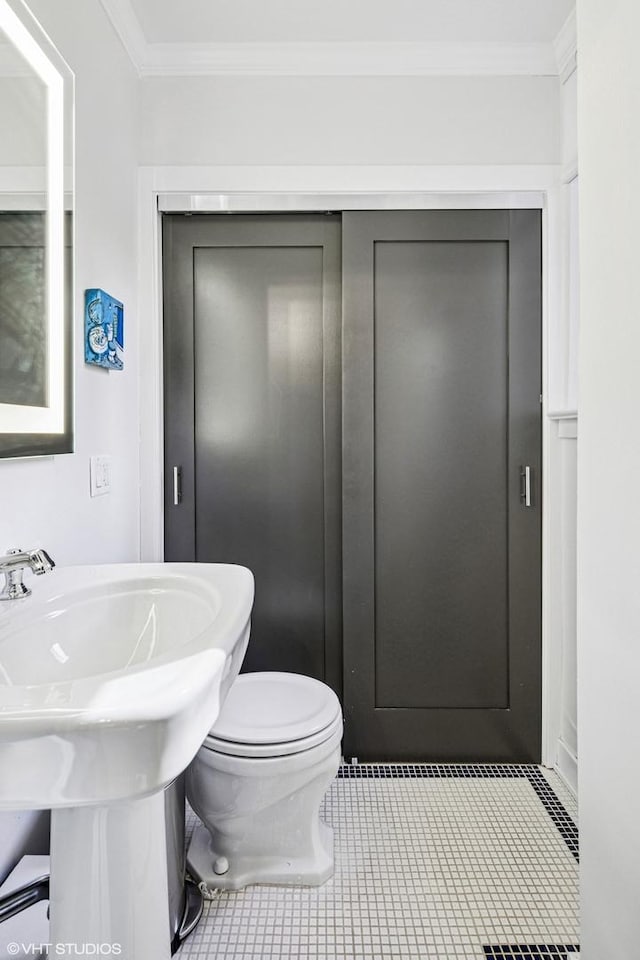 bathroom featuring tile patterned flooring, toilet, crown molding, and a sink