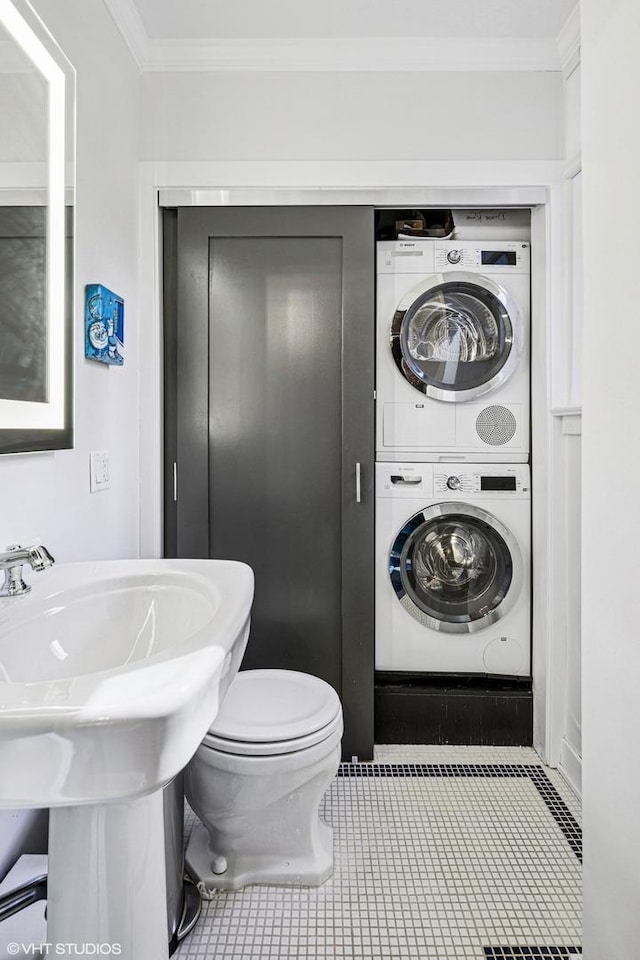 half bathroom with toilet, a sink, crown molding, tile patterned flooring, and stacked washer / drying machine