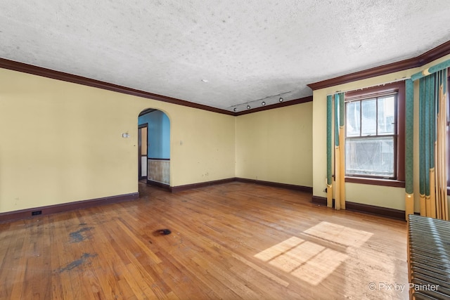 unfurnished room with arched walkways, a textured ceiling, crown molding, and hardwood / wood-style floors