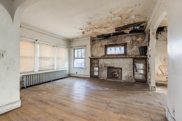 unfurnished living room with arched walkways, radiator, a fireplace, and hardwood / wood-style flooring