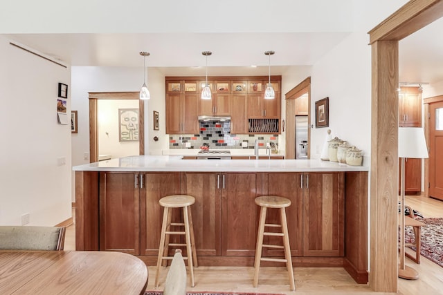 kitchen with backsplash, glass insert cabinets, a breakfast bar, light countertops, and stainless steel refrigerator with ice dispenser