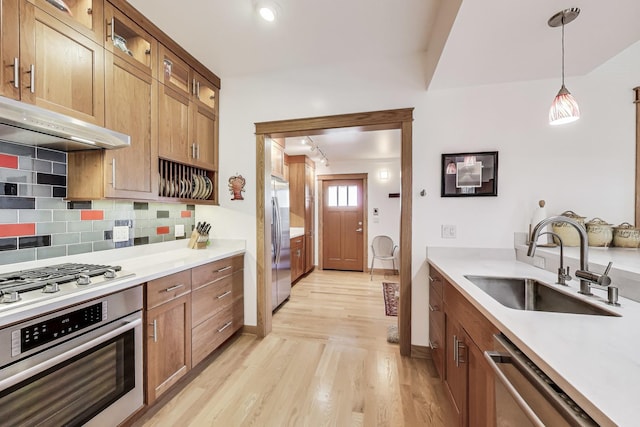 kitchen featuring a sink, decorative backsplash, stainless steel appliances, glass insert cabinets, and under cabinet range hood