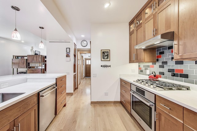 kitchen with light wood-type flooring, under cabinet range hood, decorative light fixtures, stainless steel appliances, and decorative backsplash