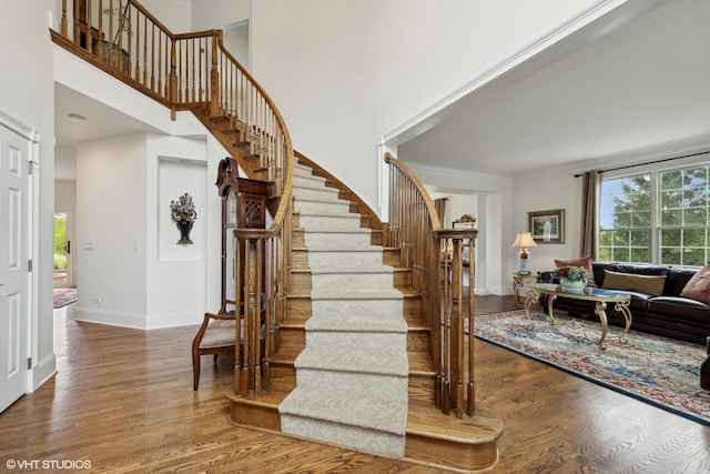 staircase featuring a high ceiling, wood finished floors, baseboards, and a healthy amount of sunlight