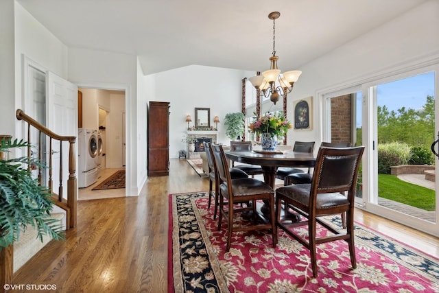 dining room featuring light wood-style flooring, a warm lit fireplace, stairway, an inviting chandelier, and washing machine and clothes dryer