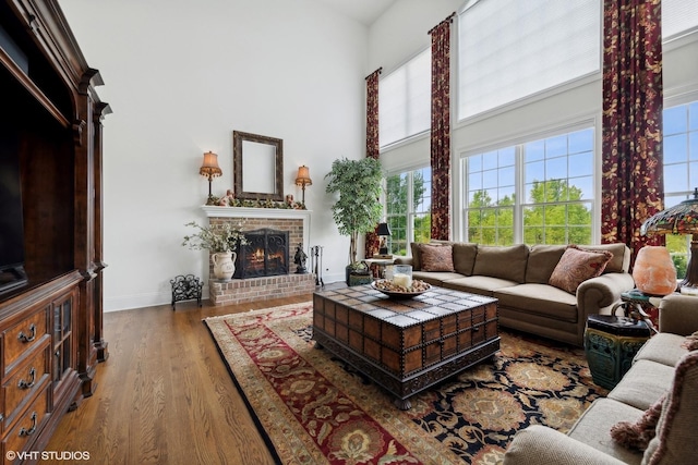 living area featuring a fireplace, baseboards, a towering ceiling, and wood finished floors