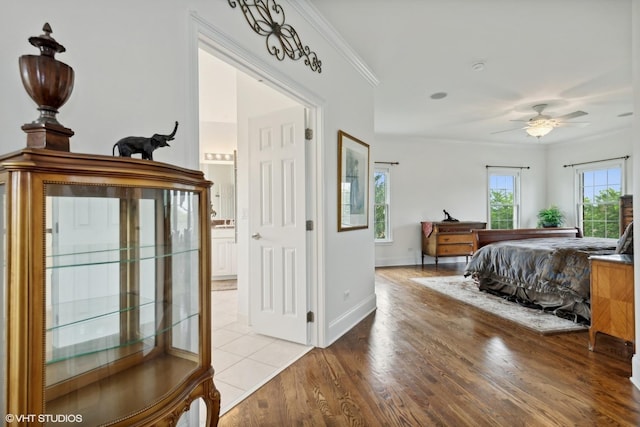 bedroom with light wood-style flooring, ensuite bathroom, baseboards, and ornamental molding