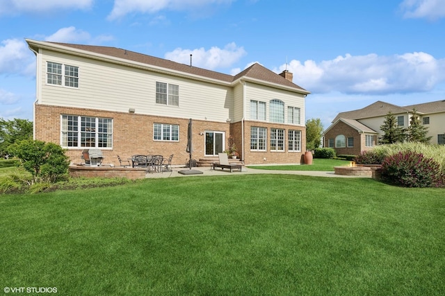 back of house with a patio, a lawn, brick siding, and a chimney