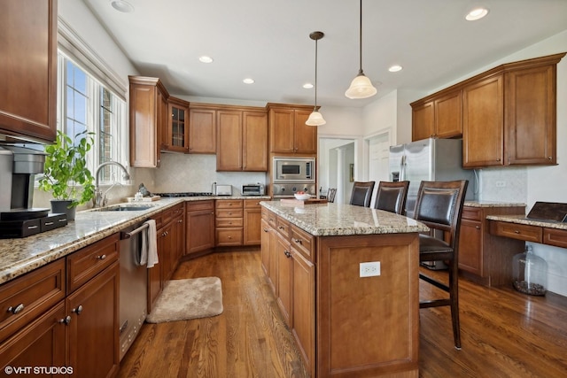 kitchen with a sink, stainless steel appliances, a kitchen island, and brown cabinetry