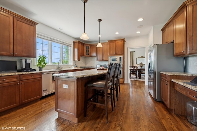 kitchen with dark wood finished floors, stainless steel appliances, decorative backsplash, a kitchen breakfast bar, and brown cabinets