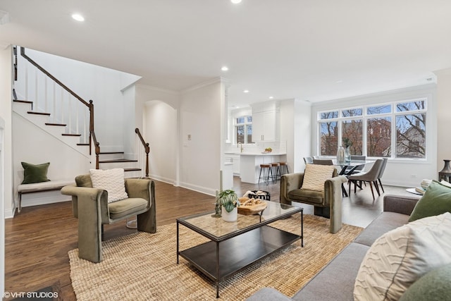 living area with ornamental molding, wood finished floors, recessed lighting, arched walkways, and stairs