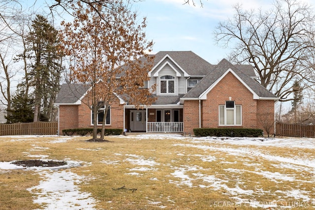 traditional-style home featuring brick siding, covered porch, a shingled roof, and fence