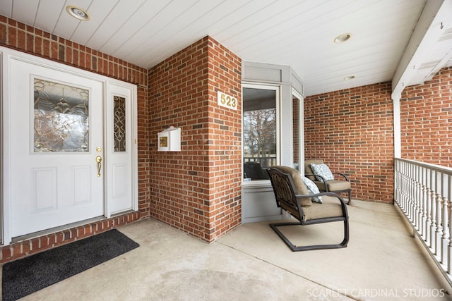 view of exterior entry featuring a porch and brick siding