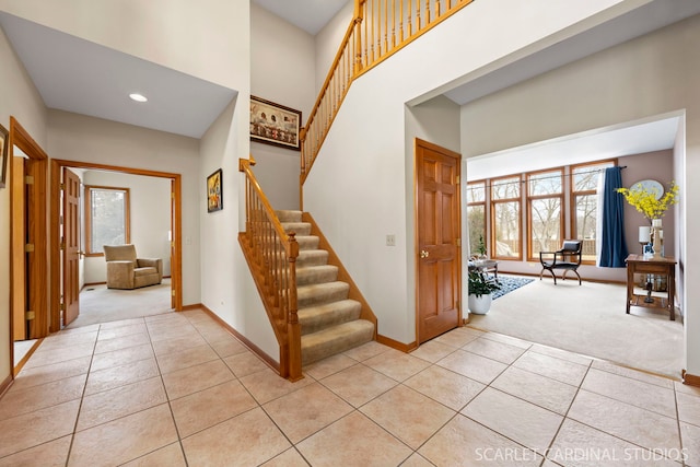 entryway featuring light tile patterned floors, baseboards, a towering ceiling, and light carpet