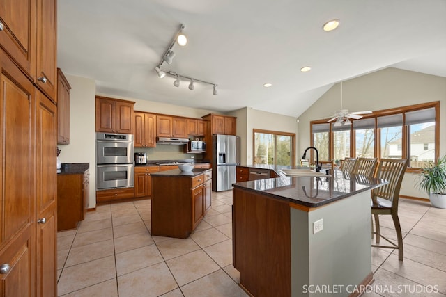 kitchen with brown cabinetry, a sink, stainless steel appliances, a large island, and under cabinet range hood