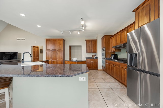 kitchen featuring a sink, under cabinet range hood, appliances with stainless steel finishes, light tile patterned floors, and a large island with sink