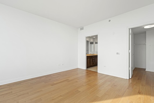 unfurnished bedroom featuring visible vents, baseboards, light wood-style flooring, and a spacious closet