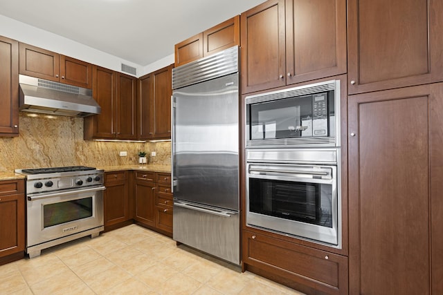 kitchen with under cabinet range hood, built in appliances, backsplash, and light stone counters